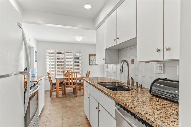 kitchen with light stone counters, a sink, decorative backsplash, white cabinets, and appliances with stainless steel finishes