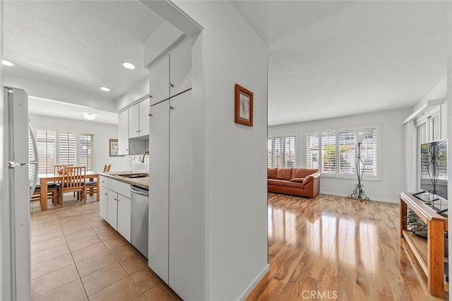 kitchen featuring stainless steel dishwasher, a sink, baseboards, white cabinetry, and freestanding refrigerator