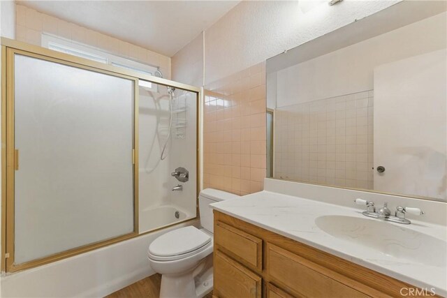 bathroom featuring wood finished floors, vanity, toilet, and bath / shower combo with glass door