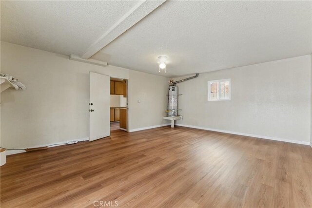 interior space featuring a textured ceiling, beamed ceiling, light wood-style flooring, secured water heater, and baseboards