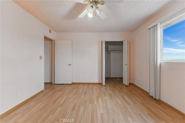 unfurnished bedroom featuring a closet, light wood-style flooring, a textured ceiling, and ceiling fan