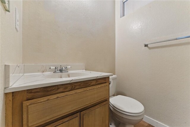 bathroom with toilet, a textured wall, vanity, and baseboards