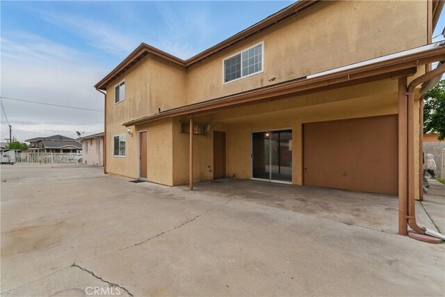 rear view of house featuring stucco siding, fence, and a patio area
