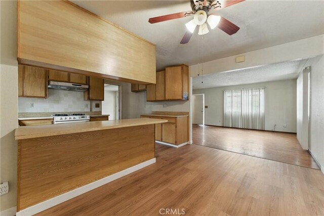 kitchen featuring brown cabinets, a peninsula, light countertops, and white range with gas stovetop