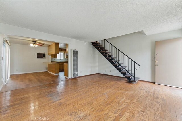 unfurnished living room featuring stairway, light wood finished floors, a heating unit, baseboards, and ceiling fan