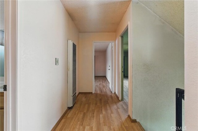 corridor with baseboards, a heating unit, a textured ceiling, and light wood-type flooring