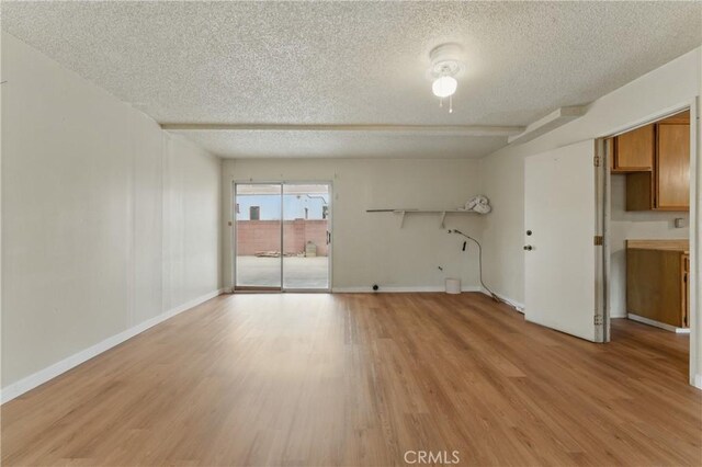 unfurnished room with light wood finished floors, baseboards, and a textured ceiling