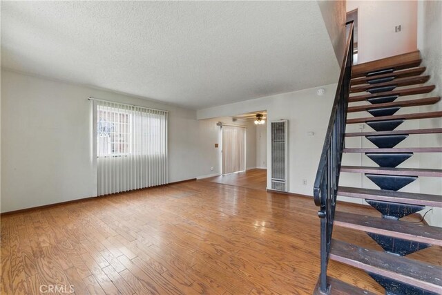 unfurnished living room with stairway, wood finished floors, a textured ceiling, and a heating unit