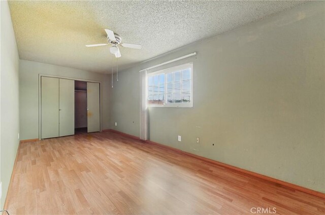 unfurnished bedroom with a ceiling fan, a textured ceiling, a closet, light wood-style flooring, and baseboards