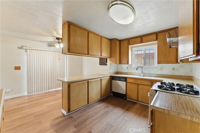 kitchen with dishwasher, a sink, light wood-style floors, a peninsula, and ceiling fan