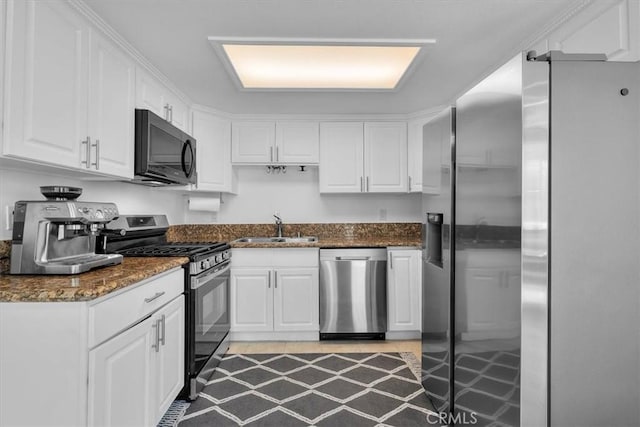 kitchen with dark stone counters, appliances with stainless steel finishes, a sink, and white cabinetry