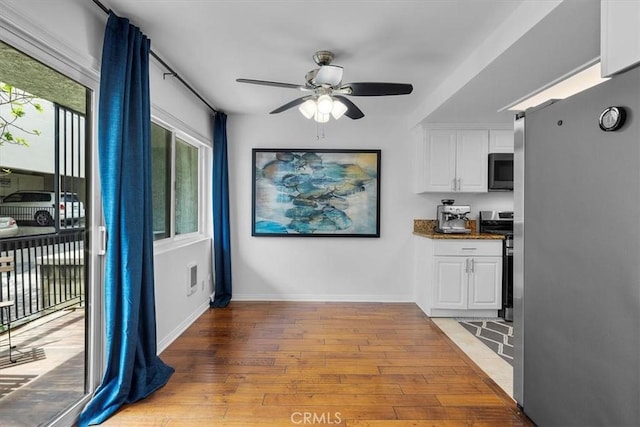 interior space featuring white cabinets, a ceiling fan, light wood-type flooring, baseboards, and electric range
