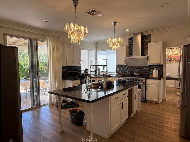 kitchen featuring an inviting chandelier, stainless steel appliances, wall chimney exhaust hood, visible vents, and white cabinets
