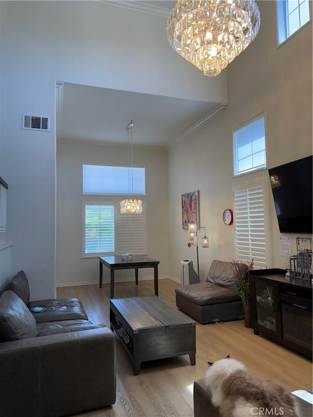living area featuring an inviting chandelier, light wood-style floors, ornamental molding, visible vents, and a towering ceiling