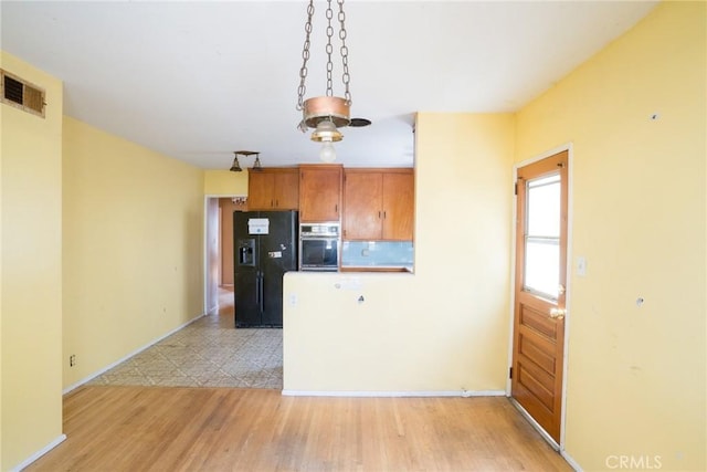kitchen featuring brown cabinetry, visible vents, light wood finished floors, black fridge, and stainless steel oven