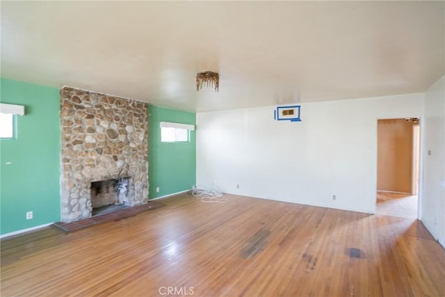 unfurnished living room featuring baseboards, a stone fireplace, and wood finished floors