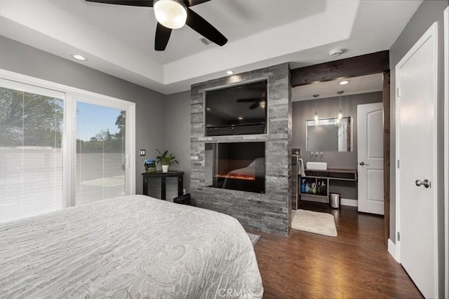 bedroom featuring visible vents, access to exterior, a stone fireplace, dark wood-type flooring, and a raised ceiling
