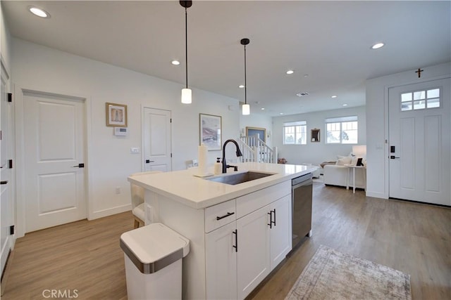 kitchen with dishwasher, a sink, light wood-style floors, open floor plan, and white cabinetry