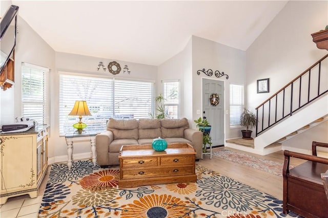 living area featuring stairs, high vaulted ceiling, baseboards, and light wood-style flooring