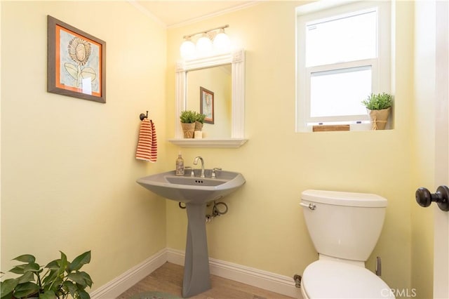 half bath with toilet, baseboards, ornamental molding, and wood finished floors