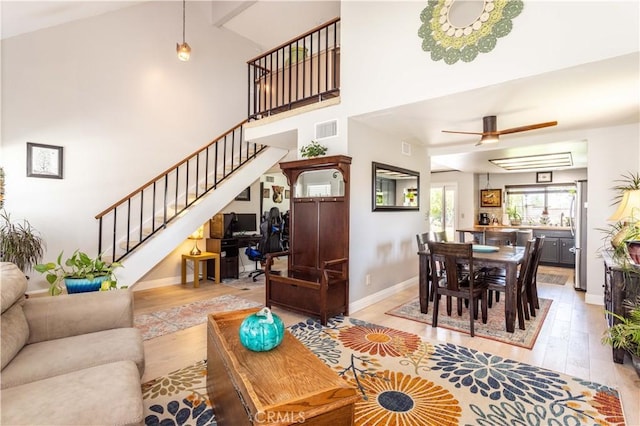 living room featuring visible vents, a ceiling fan, light wood-style floors, and stairs