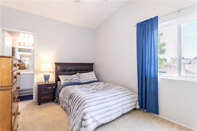 bedroom with ensuite bath, vaulted ceiling, and light carpet