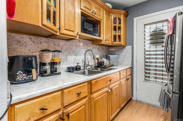 kitchen featuring a sink, black microwave, light countertops, light wood-style flooring, and freestanding refrigerator