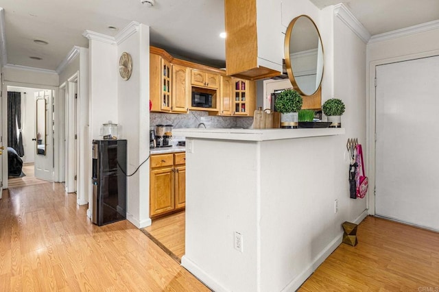 kitchen with backsplash, light wood-style floors, black microwave, crown molding, and glass insert cabinets