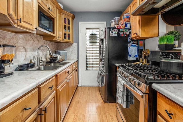 kitchen with a sink, light wood-style floors, decorative backsplash, under cabinet range hood, and appliances with stainless steel finishes
