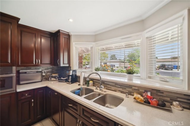 kitchen with decorative backsplash, a sink, light countertops, ornamental molding, and stainless steel oven