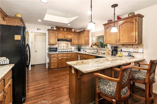 kitchen featuring under cabinet range hood, a sink, dark wood-type flooring, black appliances, and a peninsula