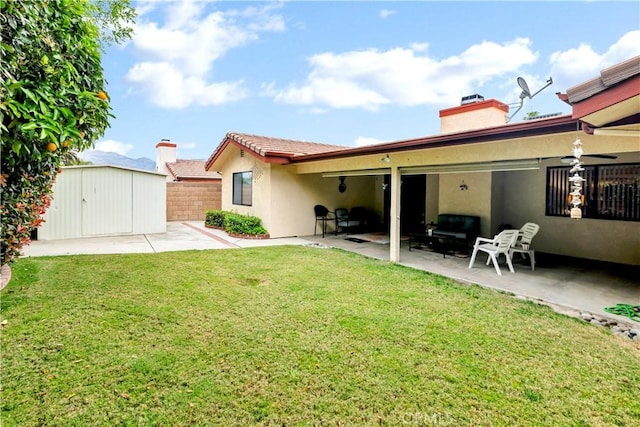 rear view of property featuring an outbuilding, fence, a yard, a shed, and a patio