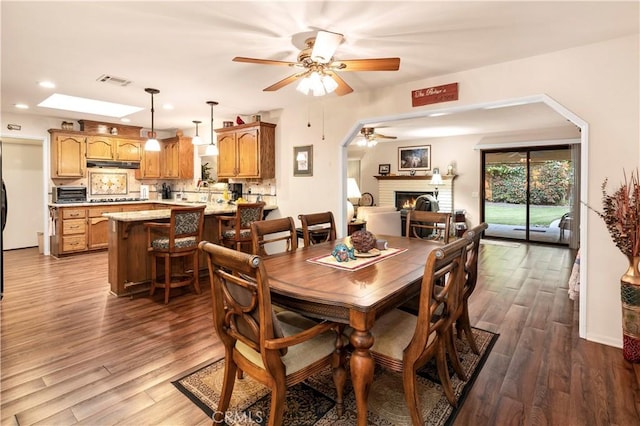 dining room featuring ceiling fan, dark wood-style flooring, a brick fireplace, visible vents, and recessed lighting