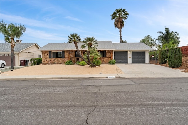 single story home featuring a garage, brick siding, concrete driveway, and fence