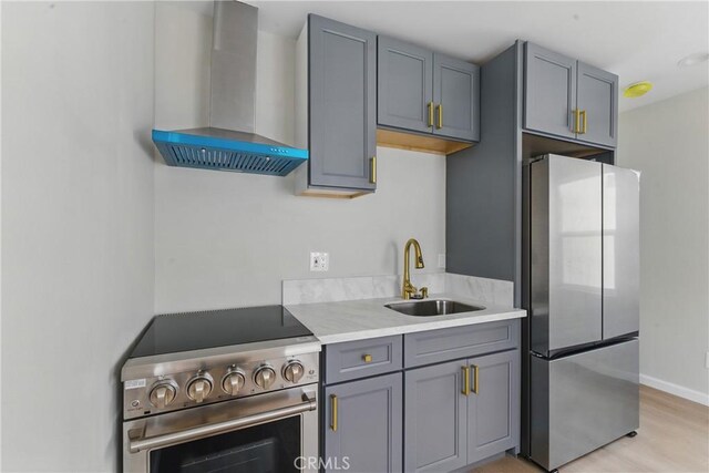 kitchen featuring stainless steel appliances, a sink, light wood-style floors, gray cabinetry, and wall chimney range hood