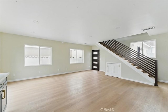 unfurnished living room featuring baseboards, visible vents, light wood finished floors, and stairs