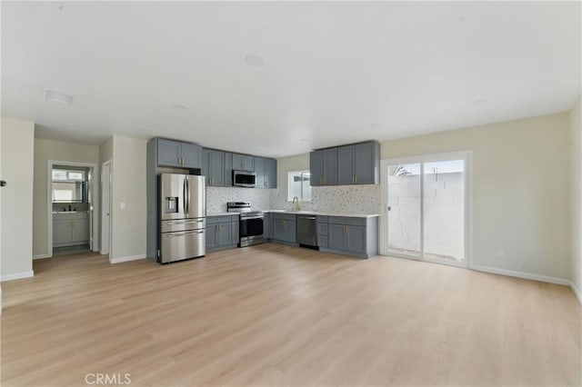 kitchen with gray cabinets, appliances with stainless steel finishes, light wood finished floors, and light countertops