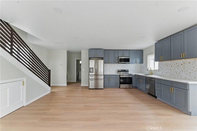 kitchen featuring light wood finished floors, stainless steel appliances, a sink, tasteful backsplash, and light countertops