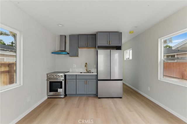 kitchen featuring stainless steel appliances, a sink, light wood-type flooring, wall chimney exhaust hood, and gray cabinetry