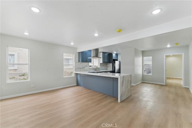 kitchen featuring light wood-style floors, light countertops, wall chimney exhaust hood, a peninsula, and freestanding refrigerator