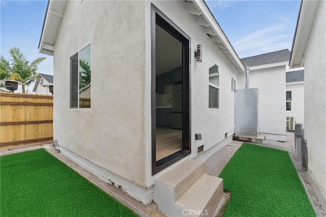 view of side of property featuring stucco siding, entry steps, roof with shingles, and fence
