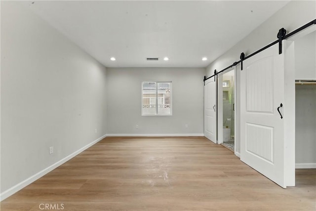 unfurnished bedroom with a barn door, recessed lighting, visible vents, light wood-style floors, and baseboards