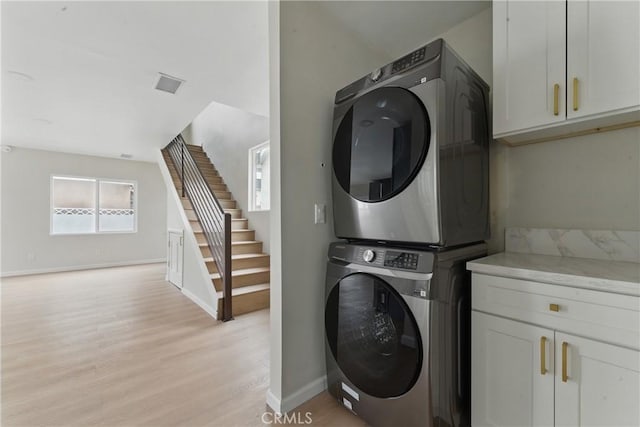 laundry room with light wood finished floors, stacked washer / dryer, visible vents, baseboards, and cabinet space