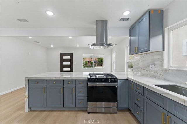 kitchen with a peninsula, island exhaust hood, light wood finished floors, and stainless steel gas range oven