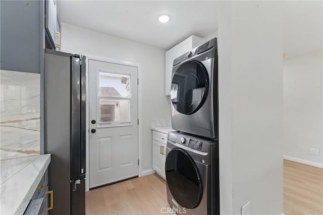 washroom featuring light wood finished floors, stacked washer and dryer, baseboards, and cabinet space