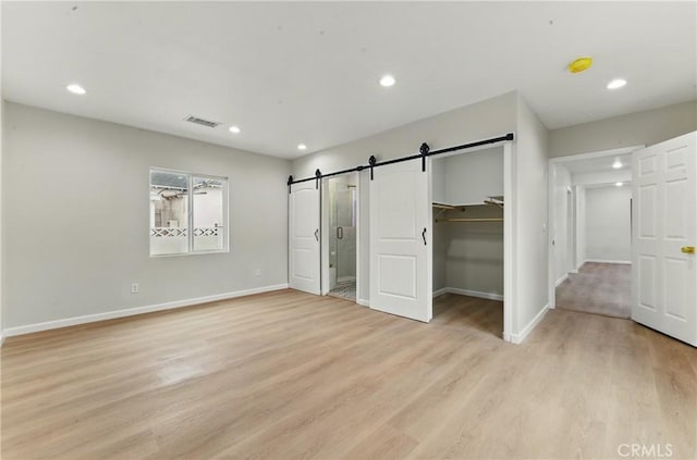 unfurnished bedroom with a barn door, light wood-style flooring, baseboards, and recessed lighting