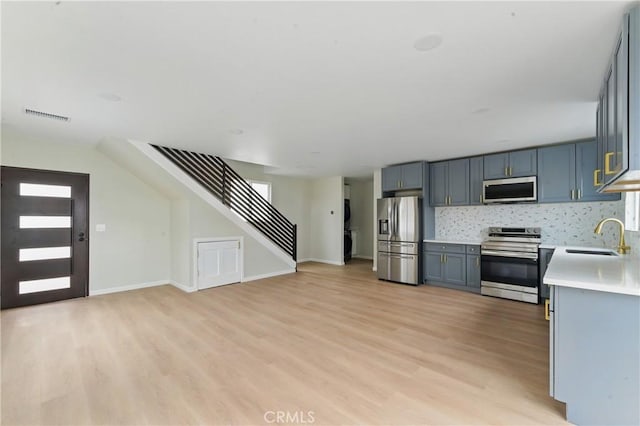 kitchen with a sink, light wood-type flooring, light countertops, appliances with stainless steel finishes, and visible vents