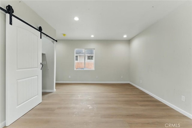 unfurnished bedroom with a barn door, baseboards, light wood-type flooring, and recessed lighting