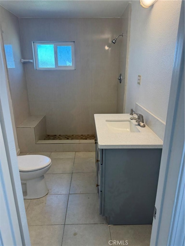bathroom featuring tile patterned flooring, a tile shower, toilet, and vanity