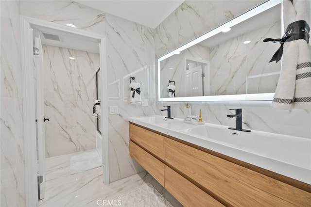 full bath with marble finish floor, double vanity, visible vents, a marble finish shower, and a sink